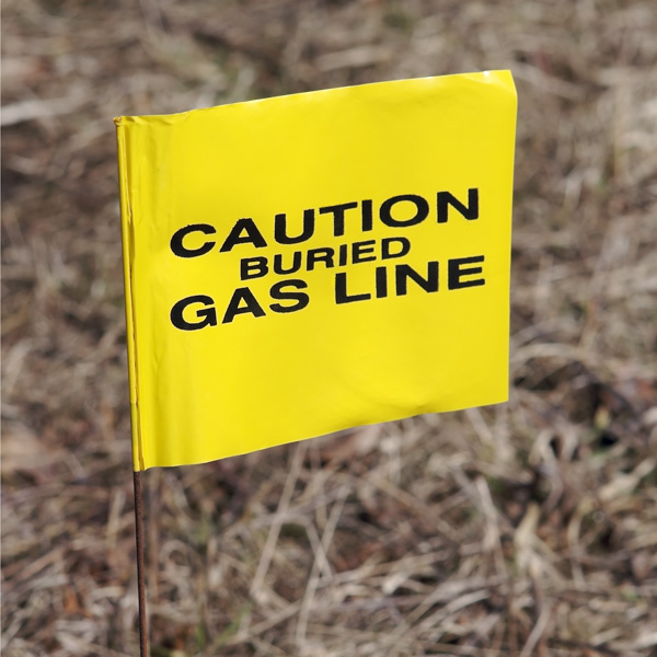 Yellow flag labeled "Caution Buried Gas Line" staked in soil
