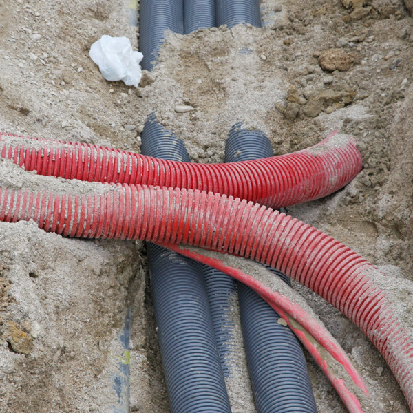 Red and black utility conduits in dirt trench
