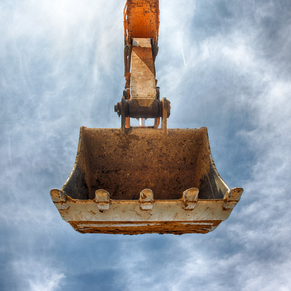 Excavator bucket raised against cloudy sky