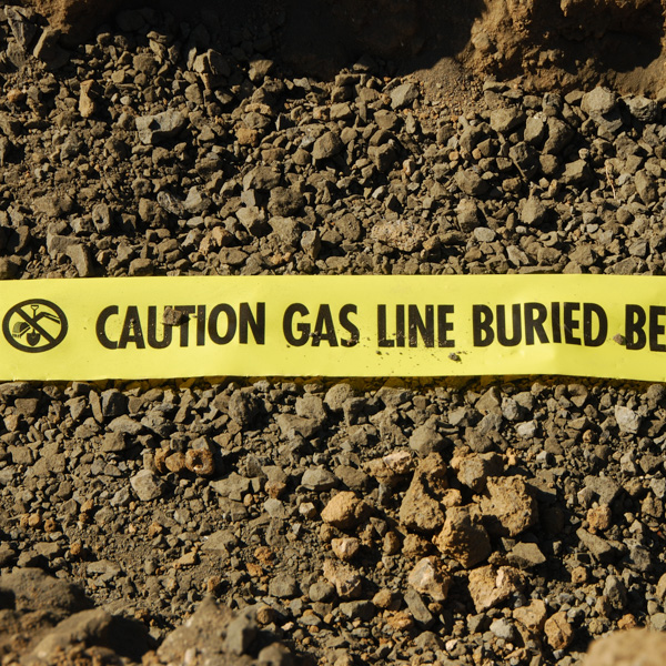 Yellow warning tape reading "Caution Gas Line Buried Below" stretched across soil